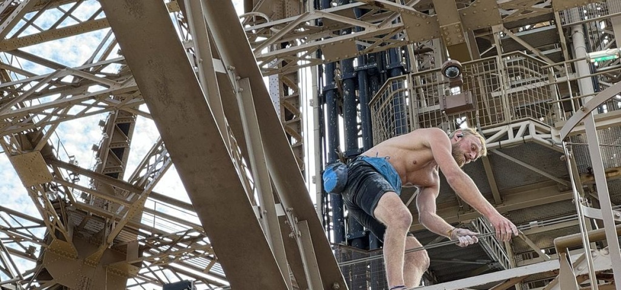 Man zonder shirt en uitrusting beklimt Eiffeltoren