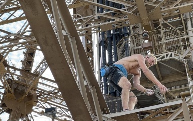 Man zonder shirt en uitrusting beklimt Eiffeltoren